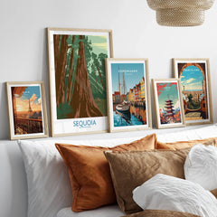 Set of five framed art prints featuring travel posters of Paris, Sequoia, Copenhagen, Tokyo, and Barcelona above a bed with neutral pillows.