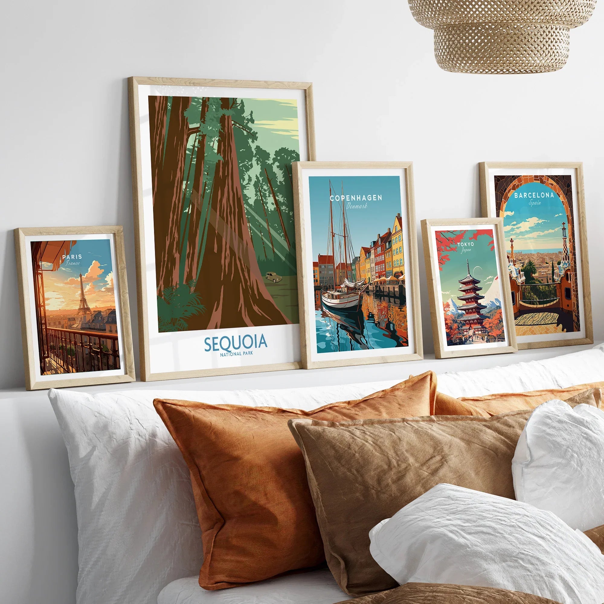 Set of five framed art prints featuring travel posters of Paris, Sequoia, Copenhagen, Tokyo, and Barcelona above a bed with neutral pillows.