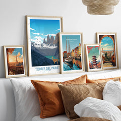 Set of five framed travel posters above a bed featuring Paris, Torres del Paine, Copenhagen, Tokyo, and Barcelona wall art.