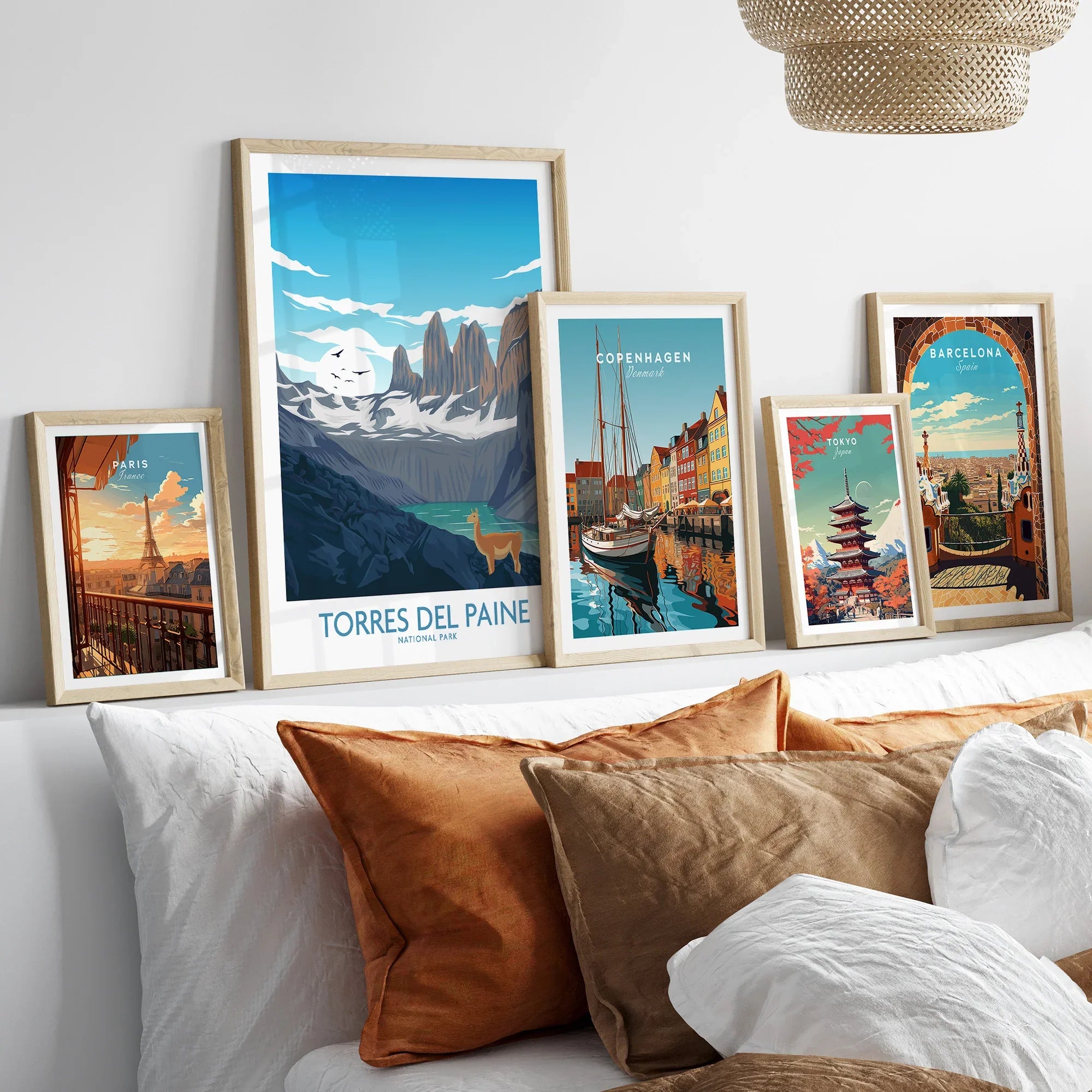 Set of five framed travel posters above a bed featuring Paris, Torres del Paine, Copenhagen, Tokyo, and Barcelona wall art.