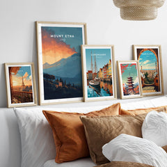 Set of five framed travel posters above a bed, featuring Paris, Mount Etna, Copenhagen, Tokyo, and Barcelona landmarks.