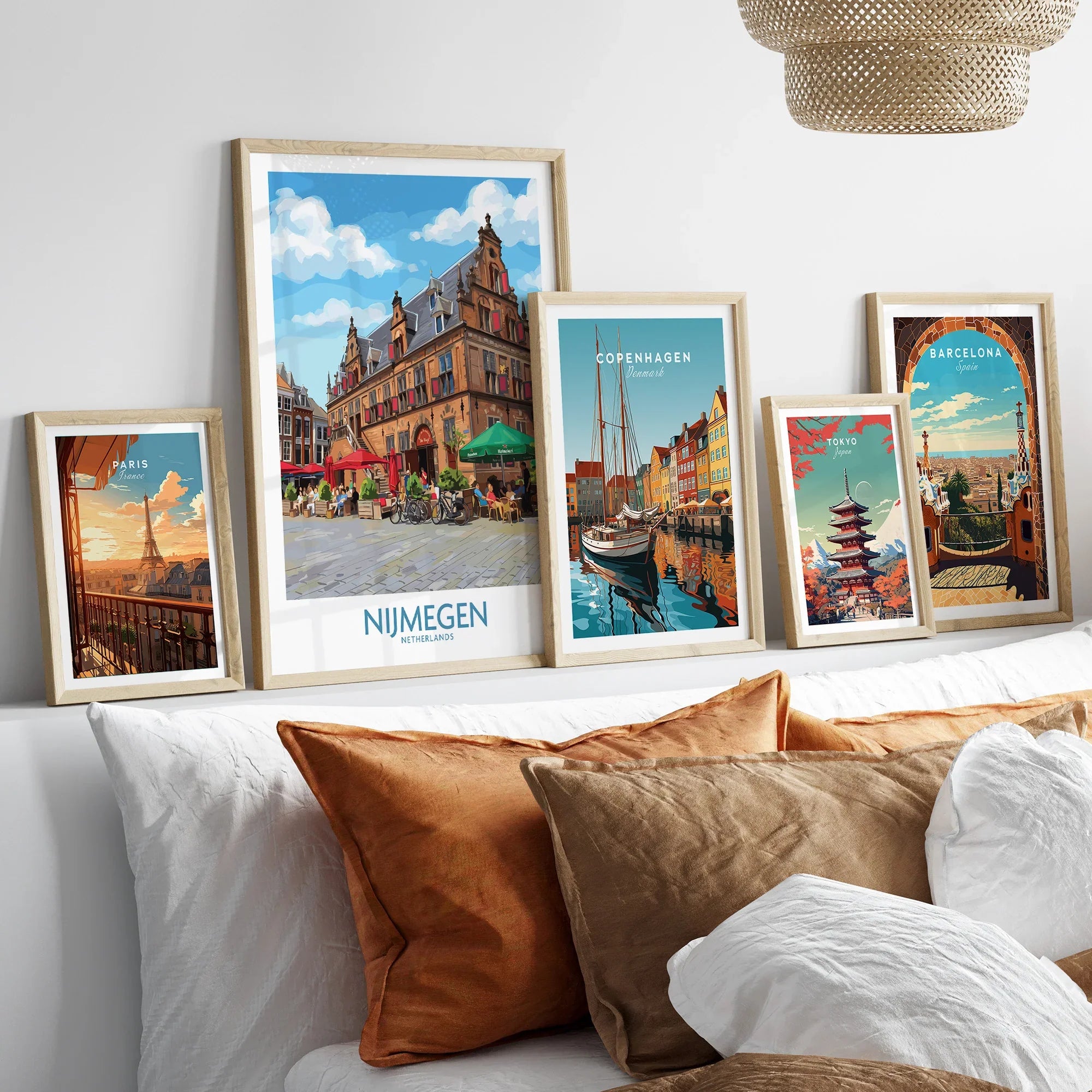 Set of five framed travel posters above bed, featuring Paris, Nijmegen, Copenhagen, Tokyo, and Barcelona skyline art prints in natural wood frames.