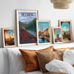 Framed travel posters featuring Paris, Olympic National Park, Copenhagen, Tokyo, and Barcelona above bed.