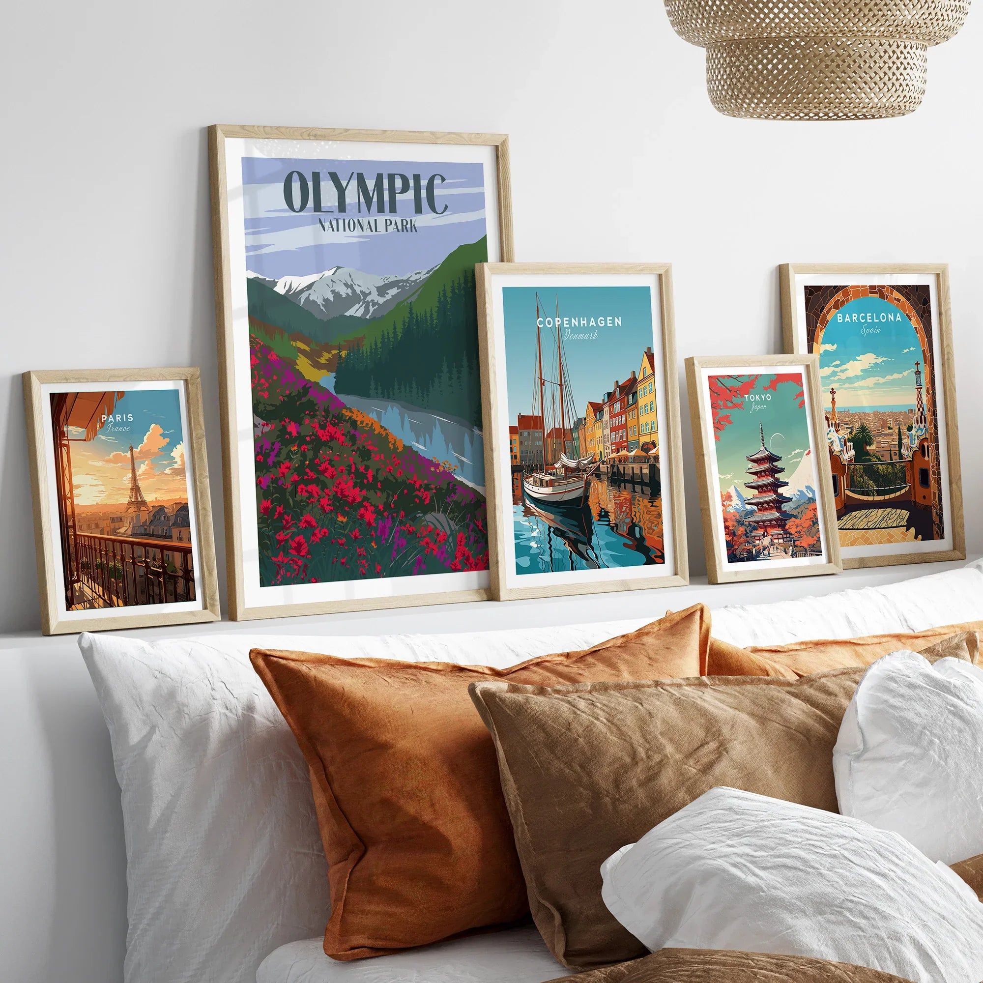 Framed travel posters featuring Paris, Olympic National Park, Copenhagen, Tokyo, and Barcelona above bed.