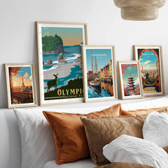 Set of five framed travel posters featuring Paris, Olympic National Park, Copenhagen, Tokyo, and Barcelona above a bed.