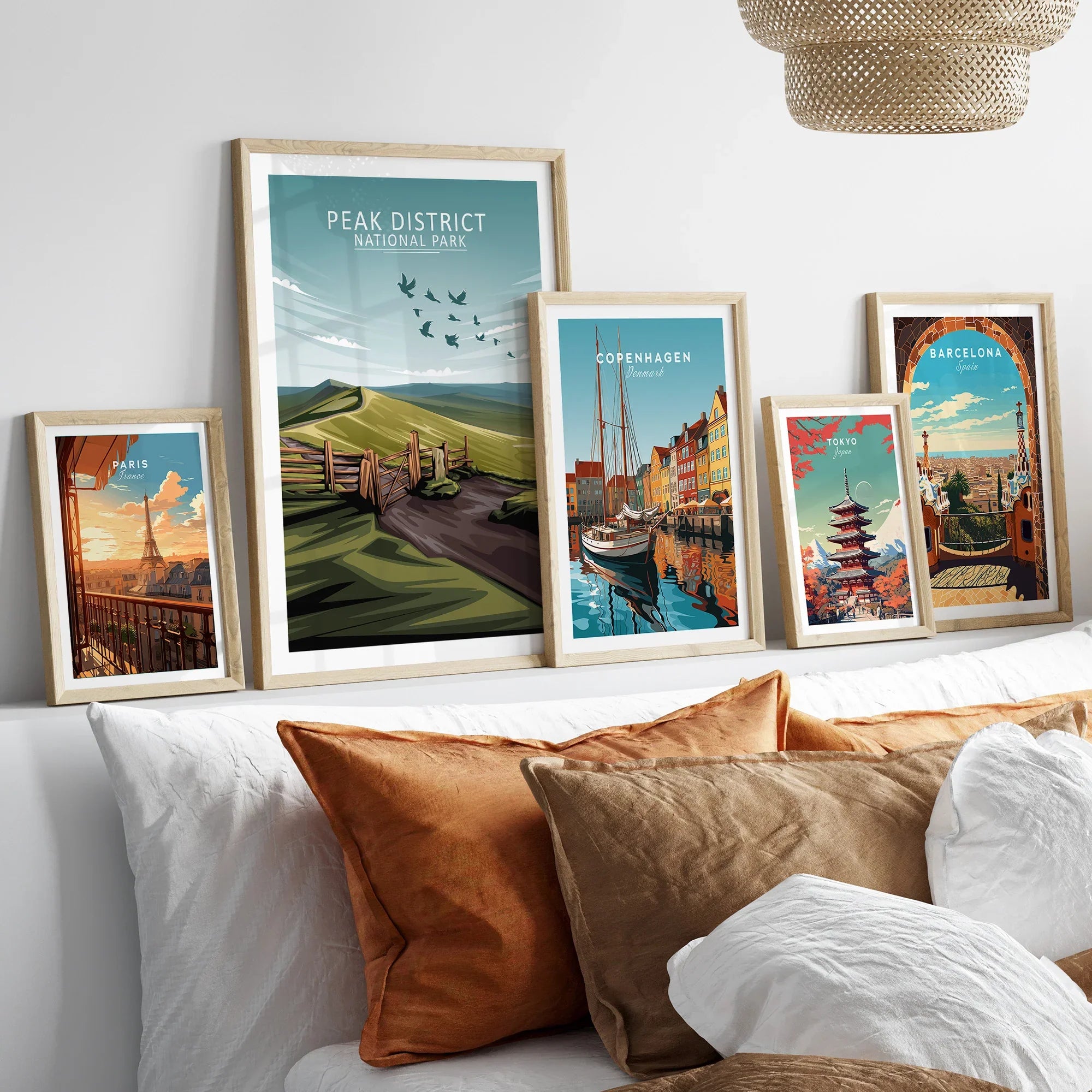 Set of five travel art prints in natural wood frames above bed, featuring Paris, Peak District, Copenhagen, Tokyo, and Barcelona.
