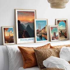 Five framed travel posters of Paris, Pico do Arieiro, Copenhagen, Tokyo, and Barcelona above a bed.