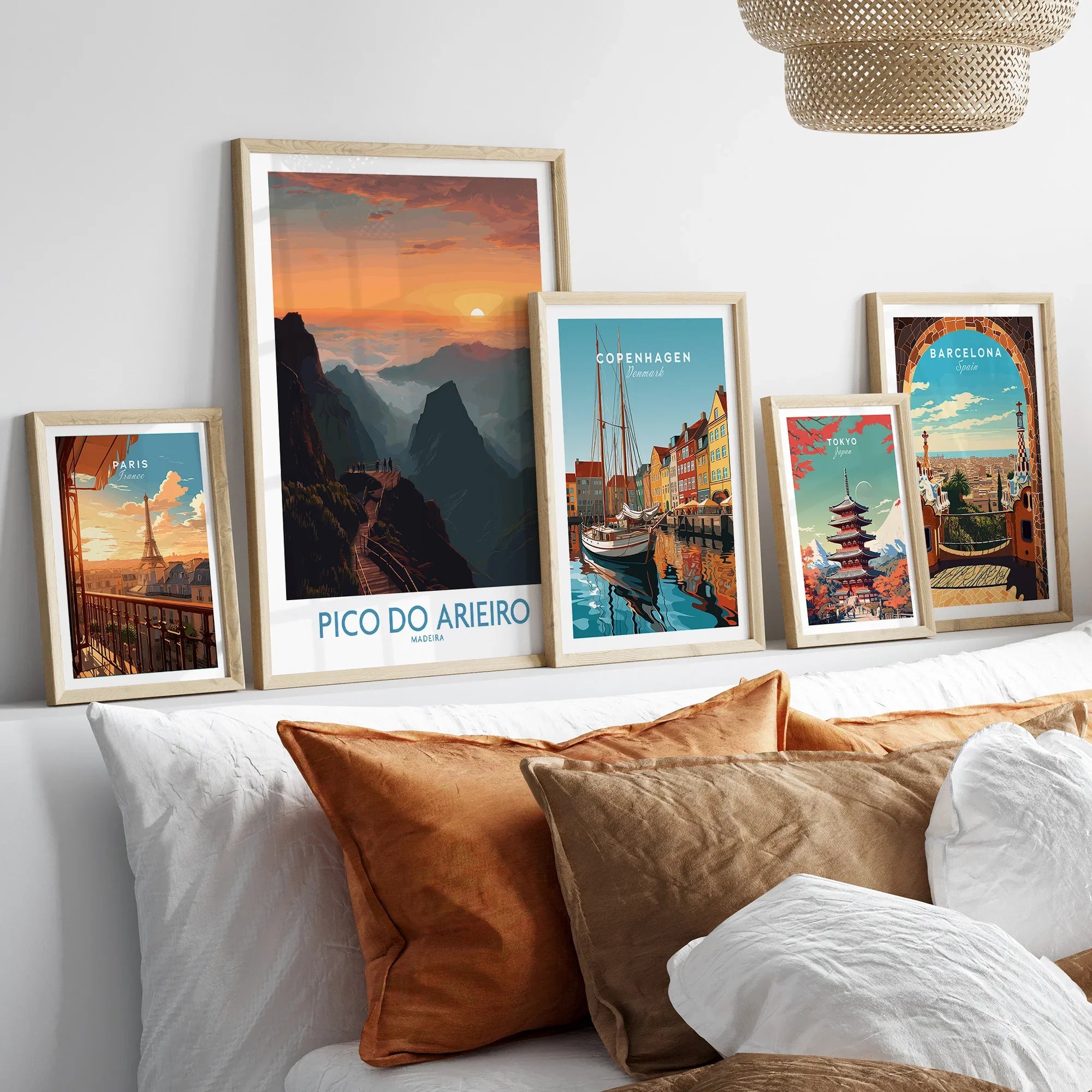 Five framed travel posters of Paris, Pico do Arieiro, Copenhagen, Tokyo, and Barcelona above a bed.