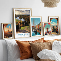 Set of five framed travel posters above a bed, featuring Paris, Richmond Hill, Copenhagen, Tokyo, and Barcelona artworks in natural wood frames.