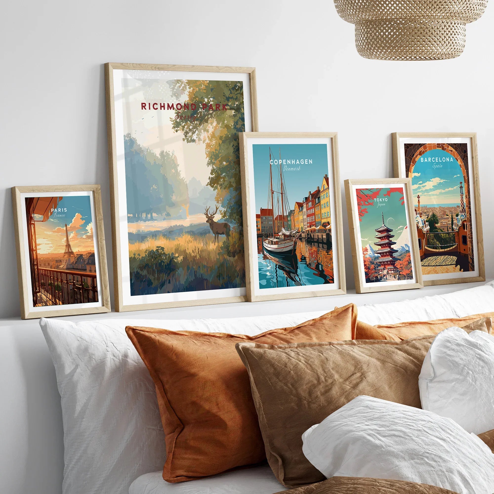 Set of five framed travel posters above bed, featuring Richmond Park, Copenhagen, Paris, Tokyo, and Barcelona with natural wood frames.