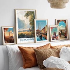 Set of five framed travel art prints featuring Richmond Park, Paris, Copenhagen, Tokyo, and Barcelona above a bed with neutral pillows.