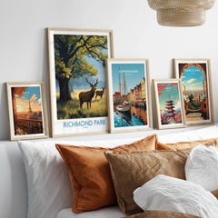Travel posters wall art set in natural wood frames above a bed, featuring Richmond Park, Paris, Copenhagen, Tokyo, and Barcelona.
