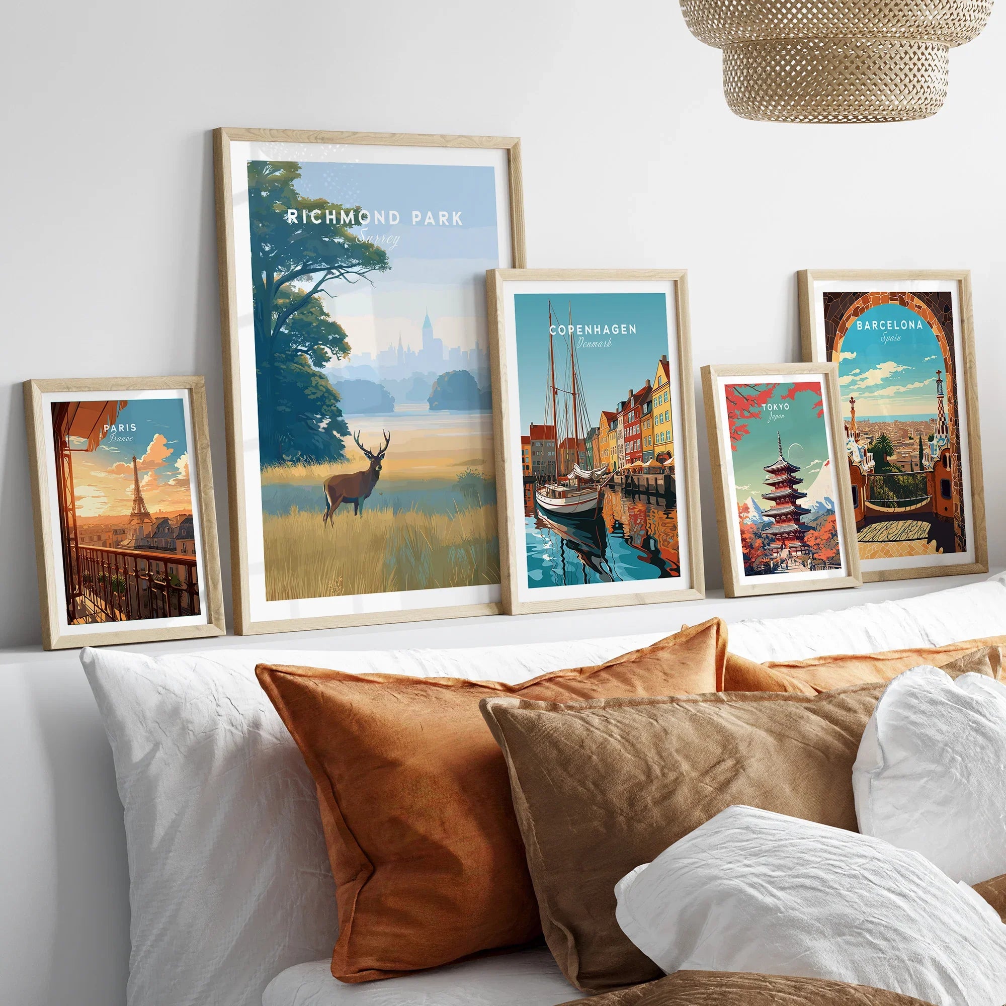 Travel art prints of Richmond Park, Paris, Copenhagen, Tokyo, Barcelona in natural wood frames above bed.