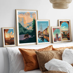 Set of five travel posters in wood frames above bed, featuring Paris, Rocky Mountains, Copenhagen, Tokyo, and Barcelona.
