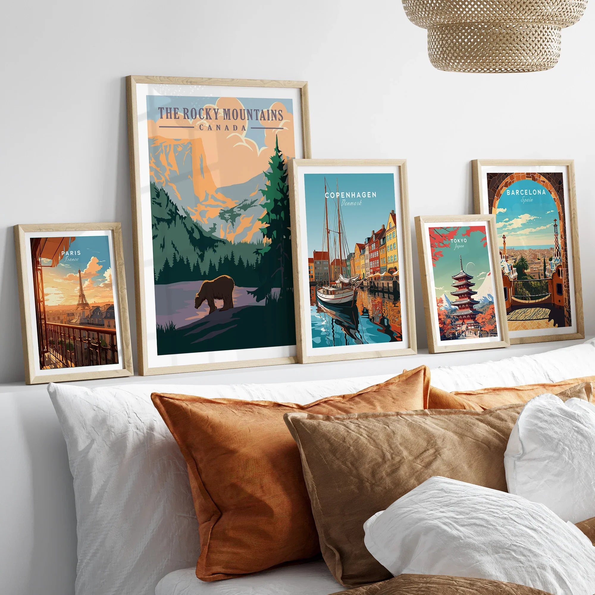 Set of five travel posters in wood frames above bed, featuring Paris, Rocky Mountains, Copenhagen, Tokyo, and Barcelona.