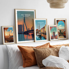 Framed travel posters of Rotterdam, Copenhagen, Paris, Tokyo, and Barcelona above a bed