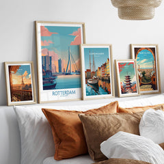 Set of five framed travel posters featuring Rotterdam, Paris, Copenhagen, Tokyo, and Barcelona above a bed with neutral pillows.