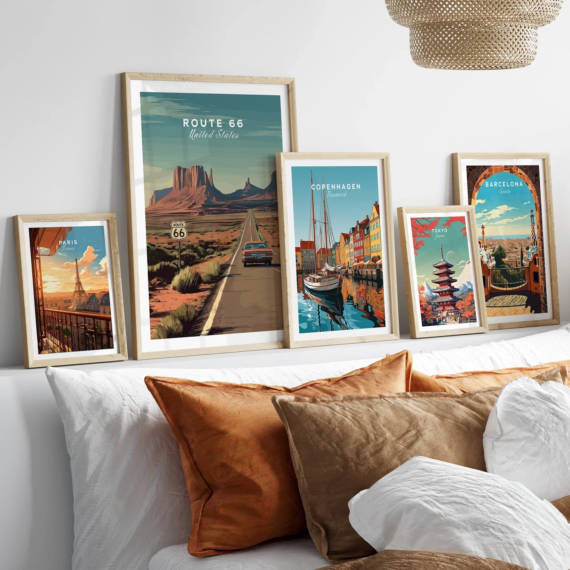 Set of five framed travel posters featuring Route 66, Paris, Copenhagen, Tokyo, and Barcelona above a bed with neutral bedding.