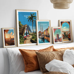 Set of five framed travel posters above a bed, featuring city and landscape prints in natural wood frames.