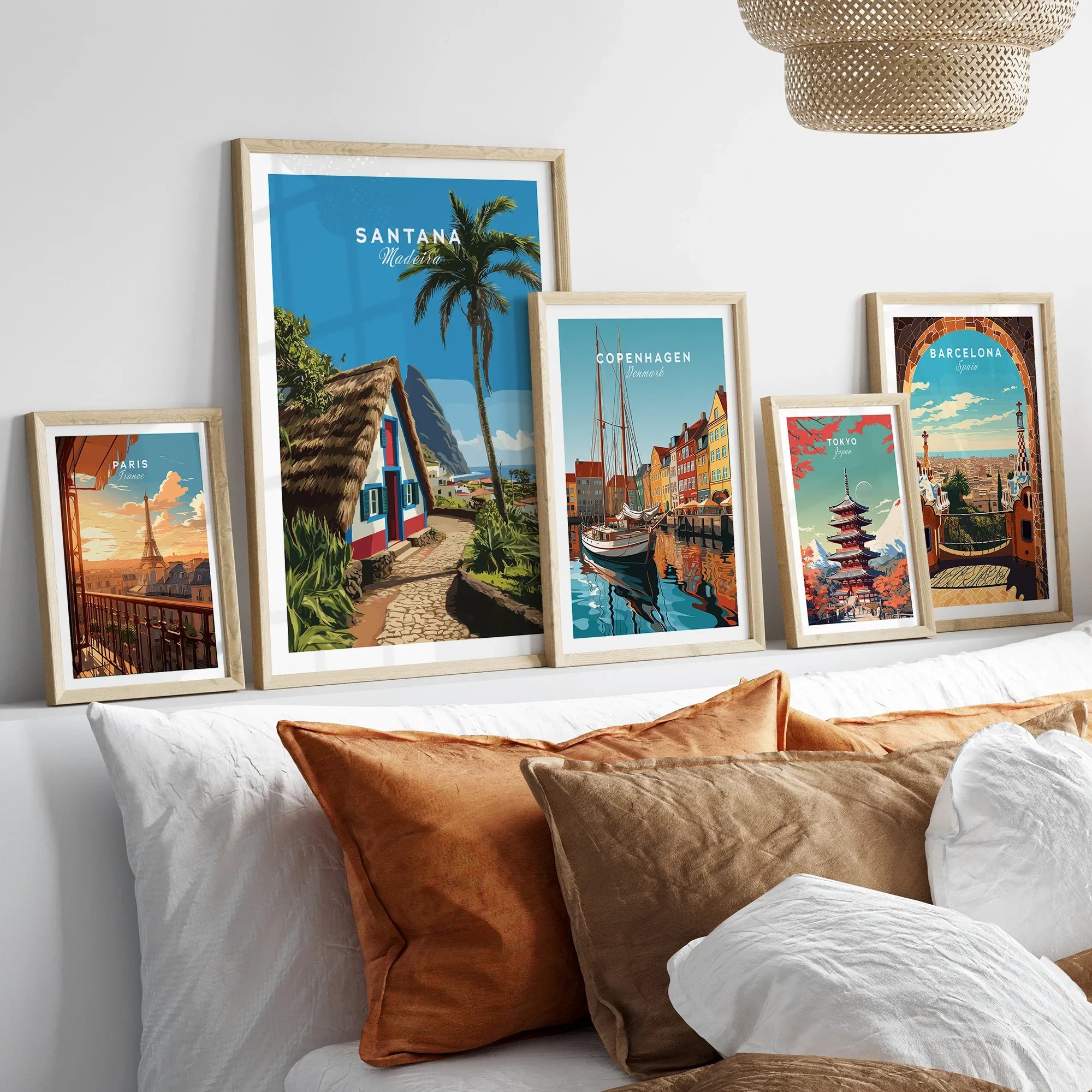 Set of five framed travel posters above a bed, featuring city and landscape prints in natural wood frames.