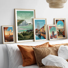 Set of five framed travel art prints of Paris, South Downs, Copenhagen, Tokyo, and Barcelona above a bed.