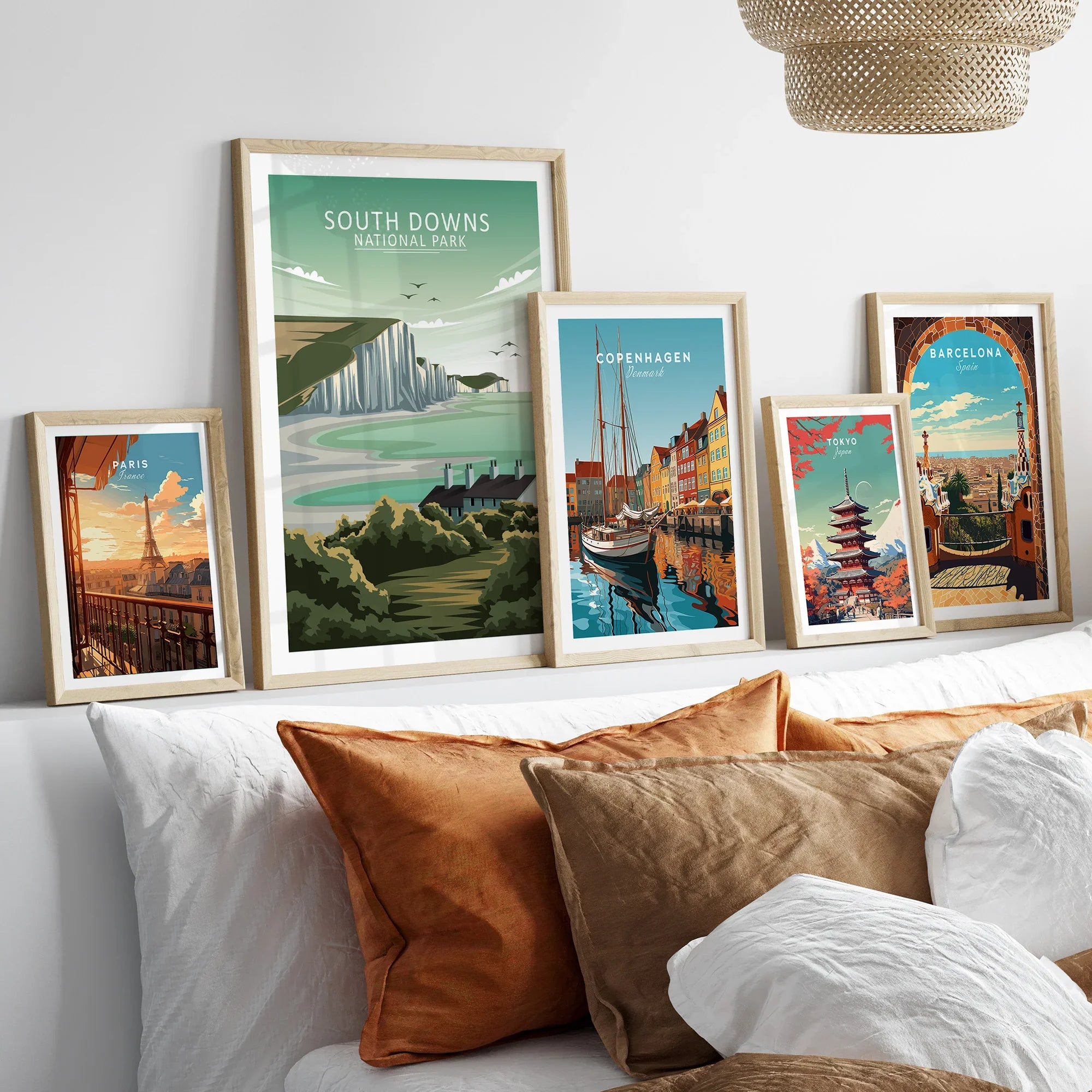 Set of five framed travel art prints of Paris, South Downs, Copenhagen, Tokyo, and Barcelona above a bed.