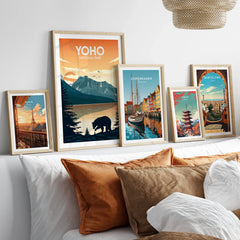 Framed travel and national park art prints above a bed with natural wood frames