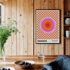 Bauhaus Exhibition Prints - Pink Circles Poster Orange Checkerboard Art framed on a wooden wall with decorative plants.