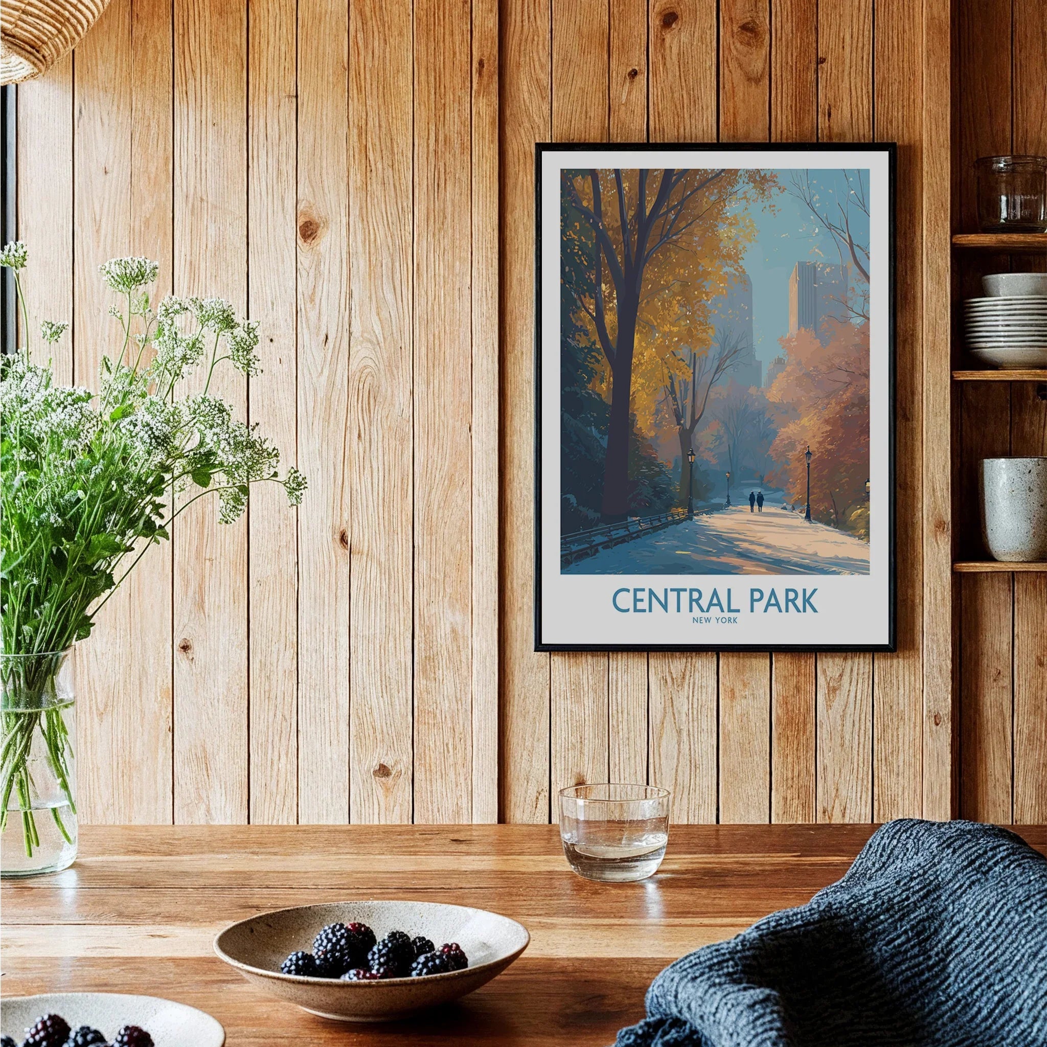 Central Park art print in black frame hangs on wooden kitchen wall above rustic table