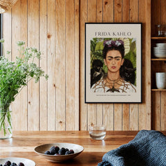 Frida Kahlo Self Portrait with Thorn Necklace and Hummingbird Print displayed on a wooden wall with plants and decor.