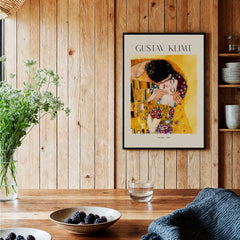 Gustav Klimt Art Print - The Kiss 1907 displayed in a cozy interior with wooden panels and plants.