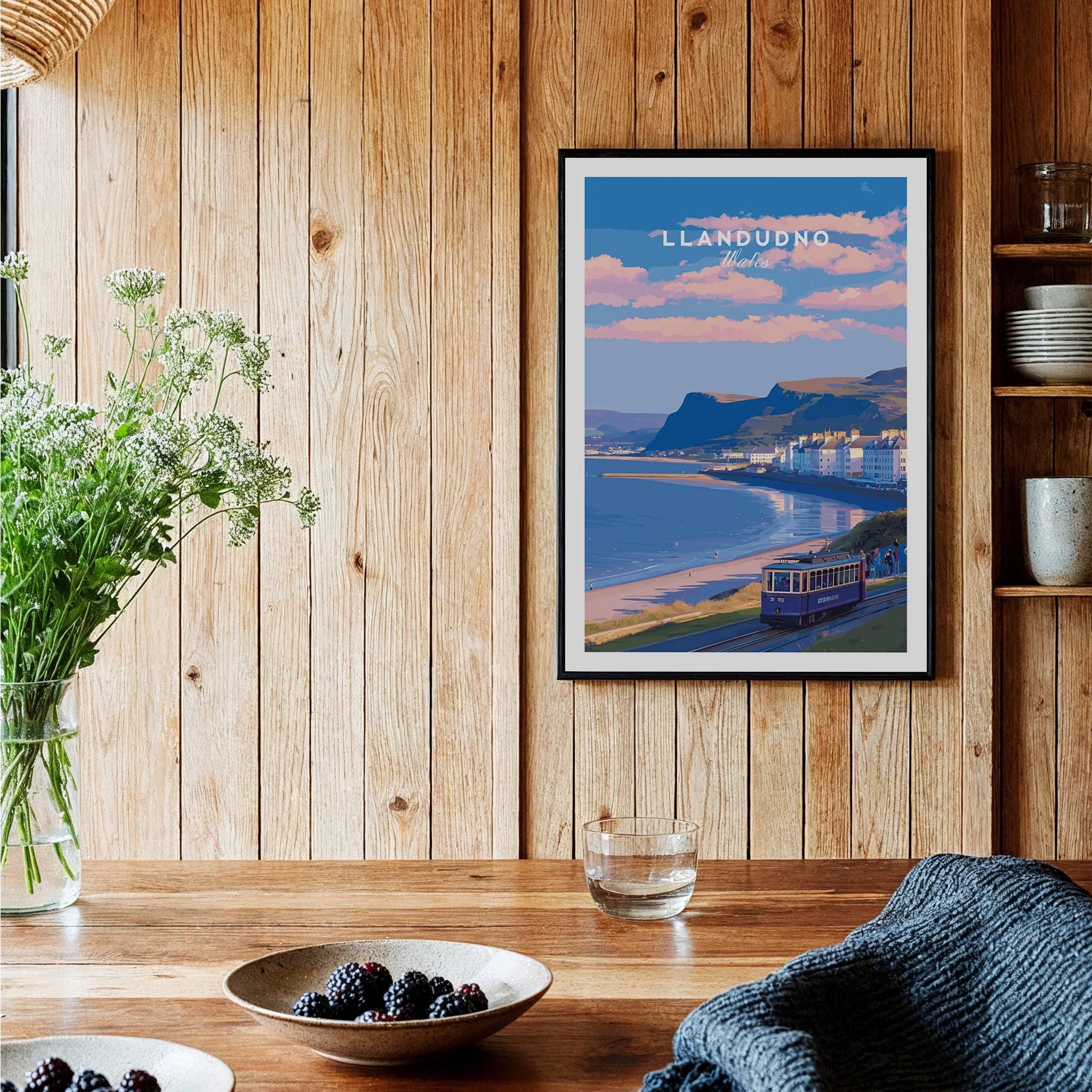 Framed Llandudno travel poster in cozy wooden kitchen with bowls of berries and wildflowers