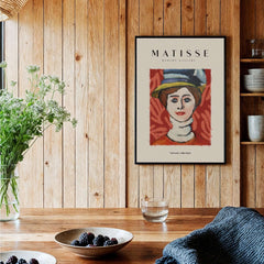 Matisse Art Prints - Woman in Elaborate Hat Portrait Poster displayed in a cozy interior with wooden accents and greenery.
