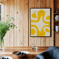 Matisse Art Prints -   Yellow Abstract Fluid Shape Poster displayed on wooden wall with plants and table decorations.
