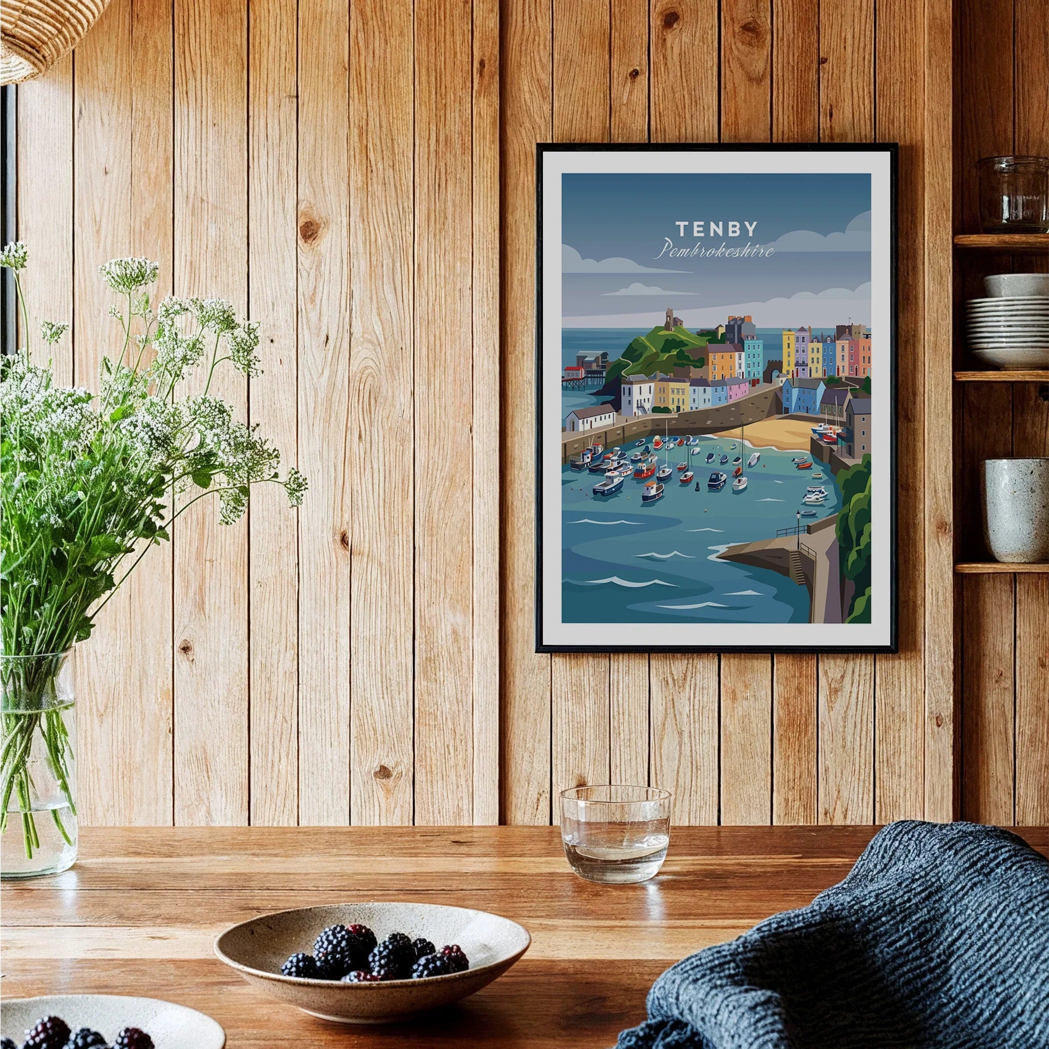 Framed Tenby travel poster art print on wooden kitchen wall, rustic decor with berries on table.
