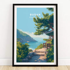 Busan South Korea travel poster art print in black frame on wooden floor, featuring coastal landscape and traditional pavilion.
