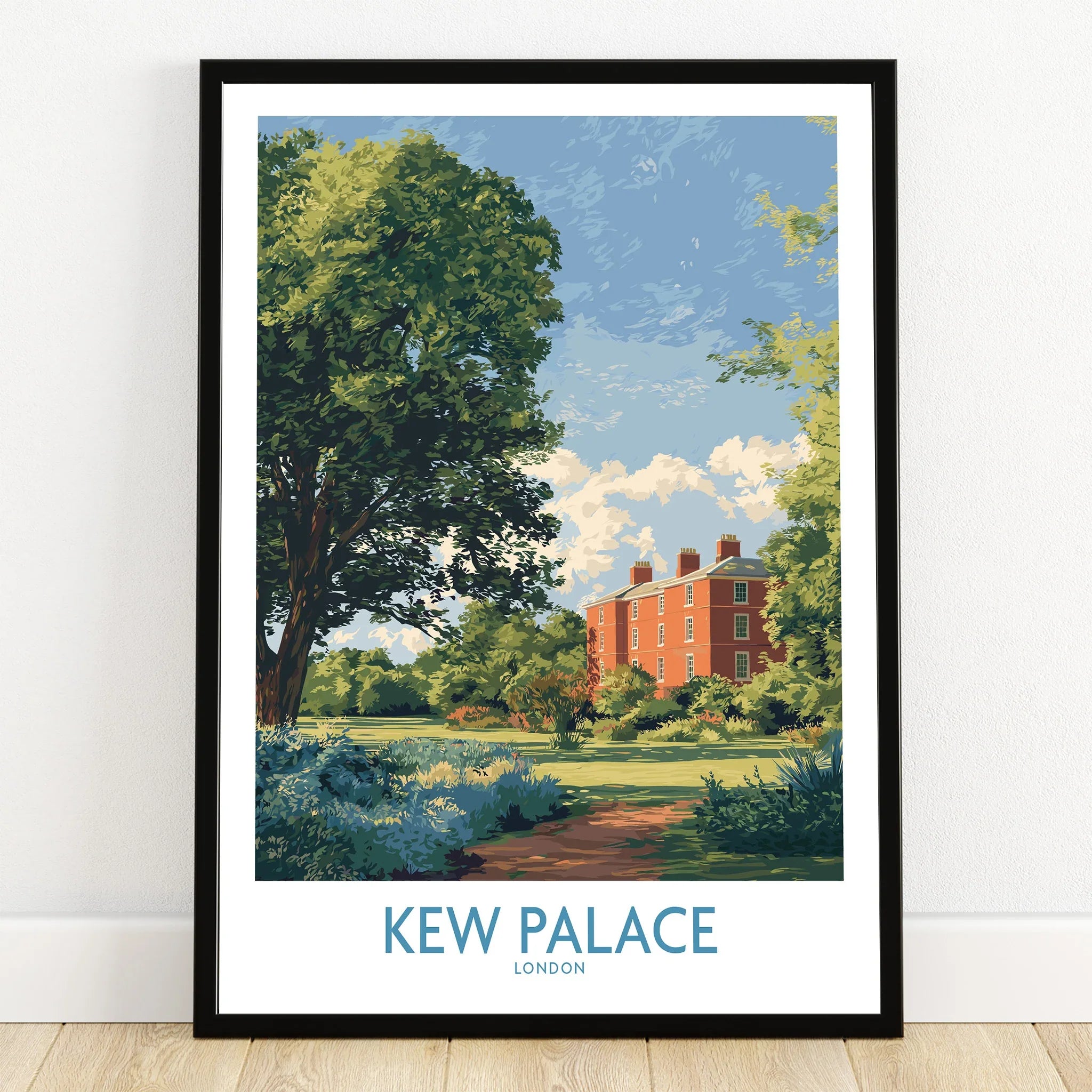 Kew Palace London art print in black frame on wooden floor, surrounded by greenery and blue sky.