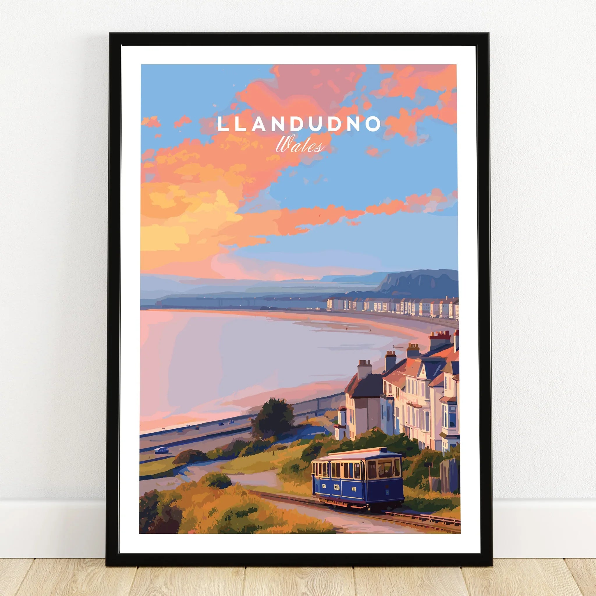Llandudno Wales travel poster art print with tram, coastal houses, and sunset in black frame.