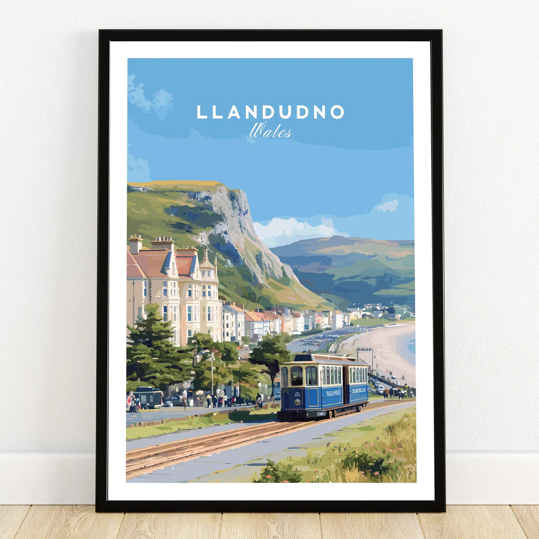 Llandudno Wales art print in black frame, featuring tram, beach, and mountains on wooden floor.