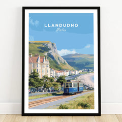 Llandudno Wales art print in black frame, featuring tram, beach, and mountains on wooden floor.