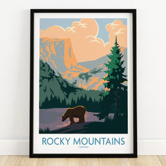 Rocky Mountains Canada art print with bear, pine trees, and sunset in black frame on floor