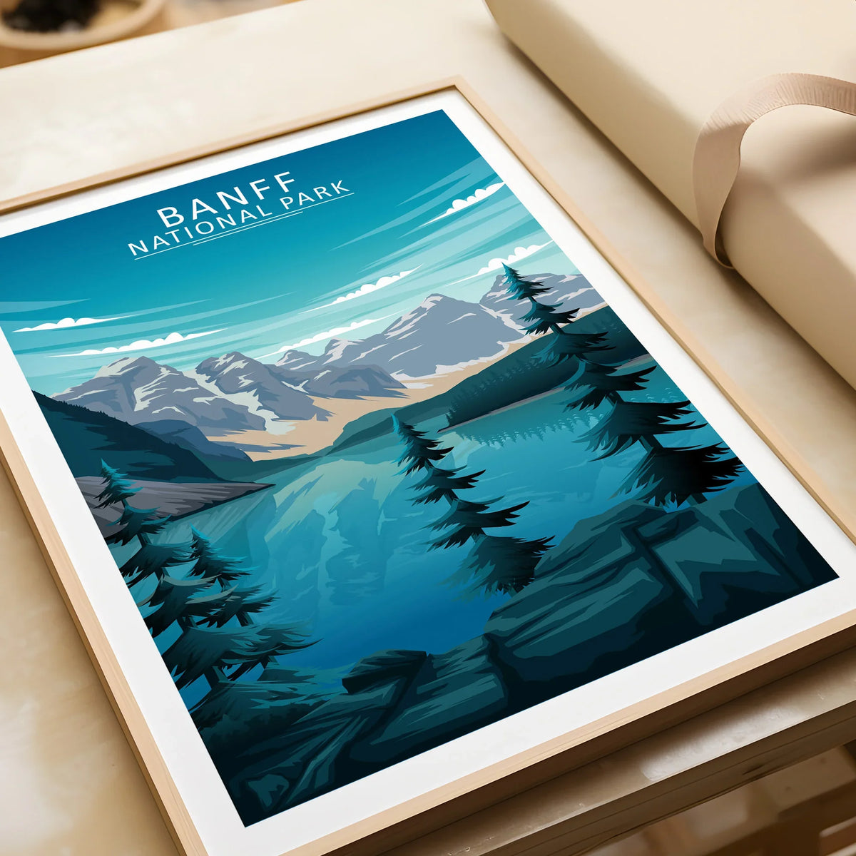 Framed Banff National Park art print with mountains, lake, and pine trees, unwrapped on table