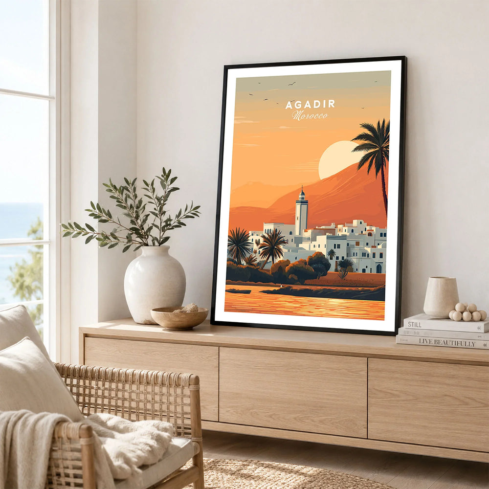 Agadir Travel Poster – Moroccan Mosque and Desert Sunset Art in a black frame displayed on an oak sideboard in a bright coastal living room