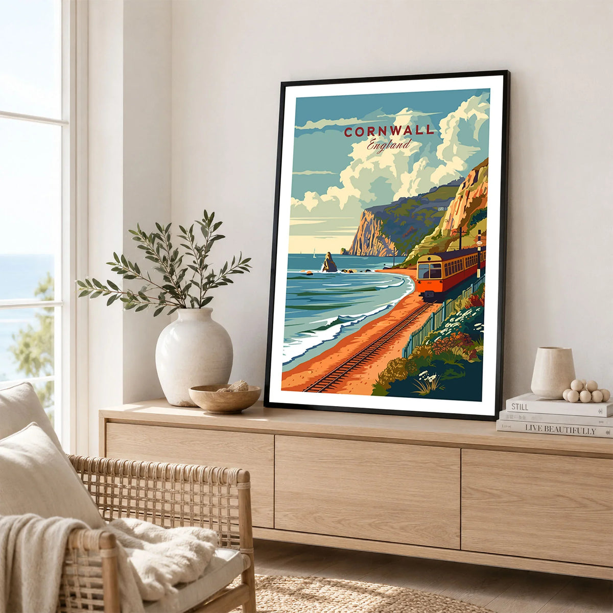 Cornwall Coast Travel Print in a black frame displayed on an oak sideboard in a bright coastal living room
