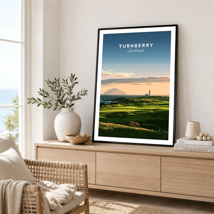 Turnberry Scotland Ailsa Craig Travel Poster — Ailsa Craig and the white lighthouse across rolling coastal turf at dusk, shown as framed artwork living room lifestyle setting