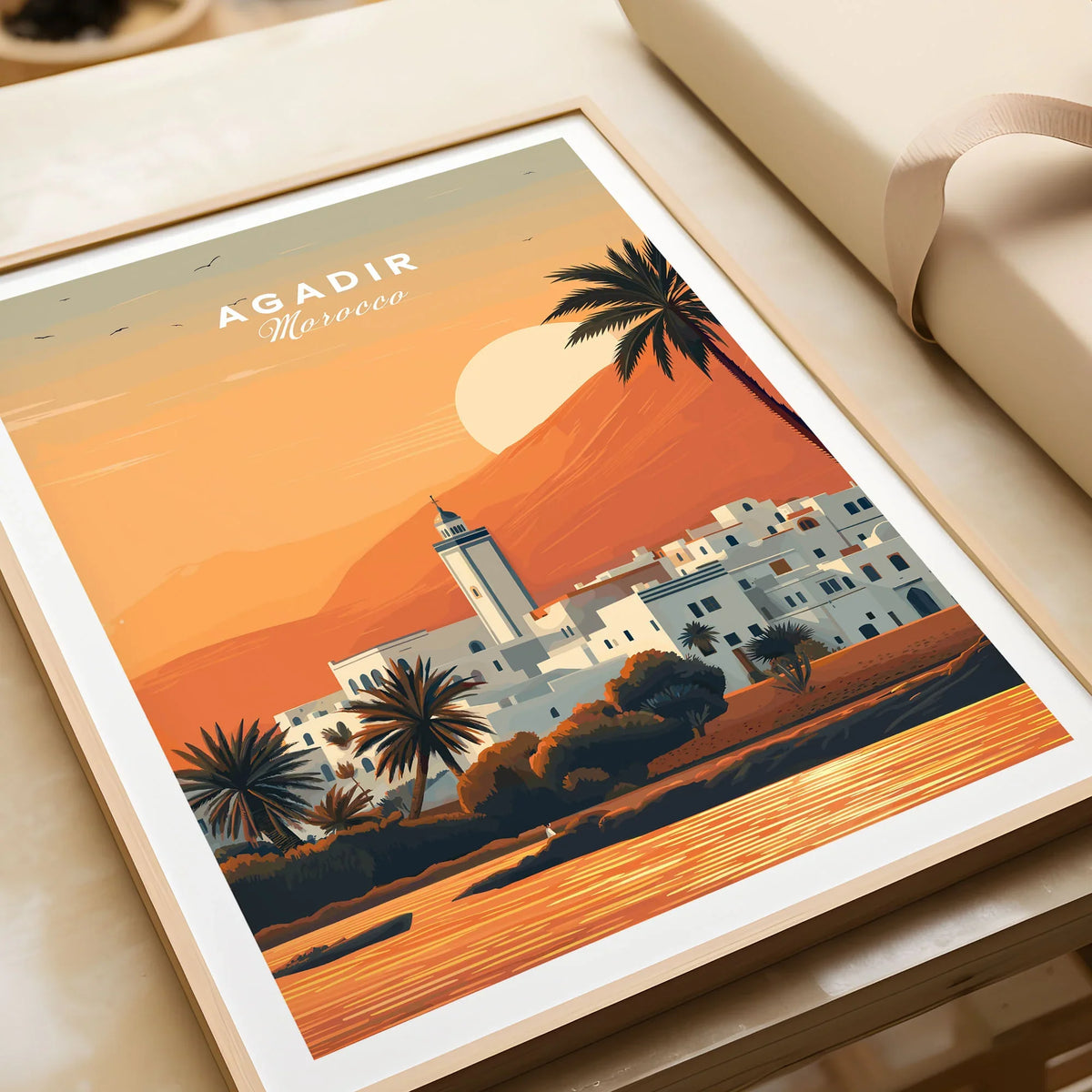 Agadir Travel Poster – Moroccan Mosque and Desert Sunset Art in a natural wood frame beside wrapped gift packaging, close-up detail