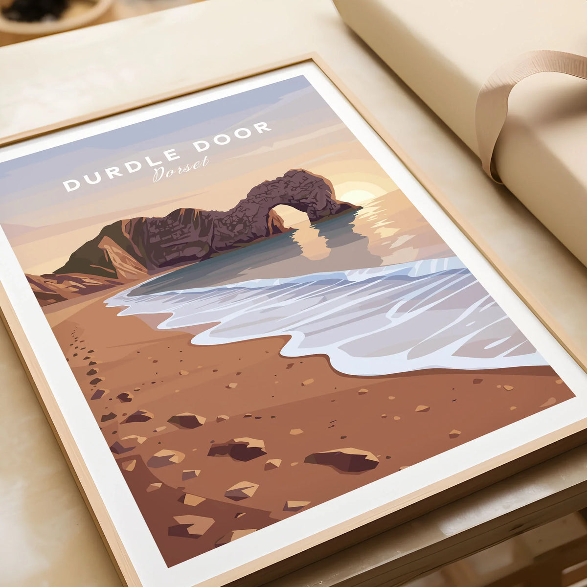 Durdle Door Travel Poster – Jurassic Coast Sunset Art in a natural wood frame beside wrapped gift packaging, close-up detail