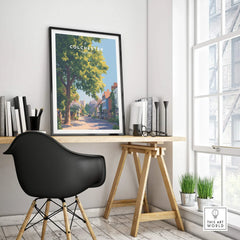 Framed Colchester travel poster on modern office desk with black chair and books.
