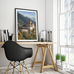 Framed Vaduz city travel poster on modern office desk near black chair and window