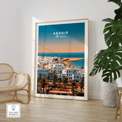 Agadir Travel Poster – City Skyline in a large natural wood frame leaning in a room with a rattan chair and monstera plant